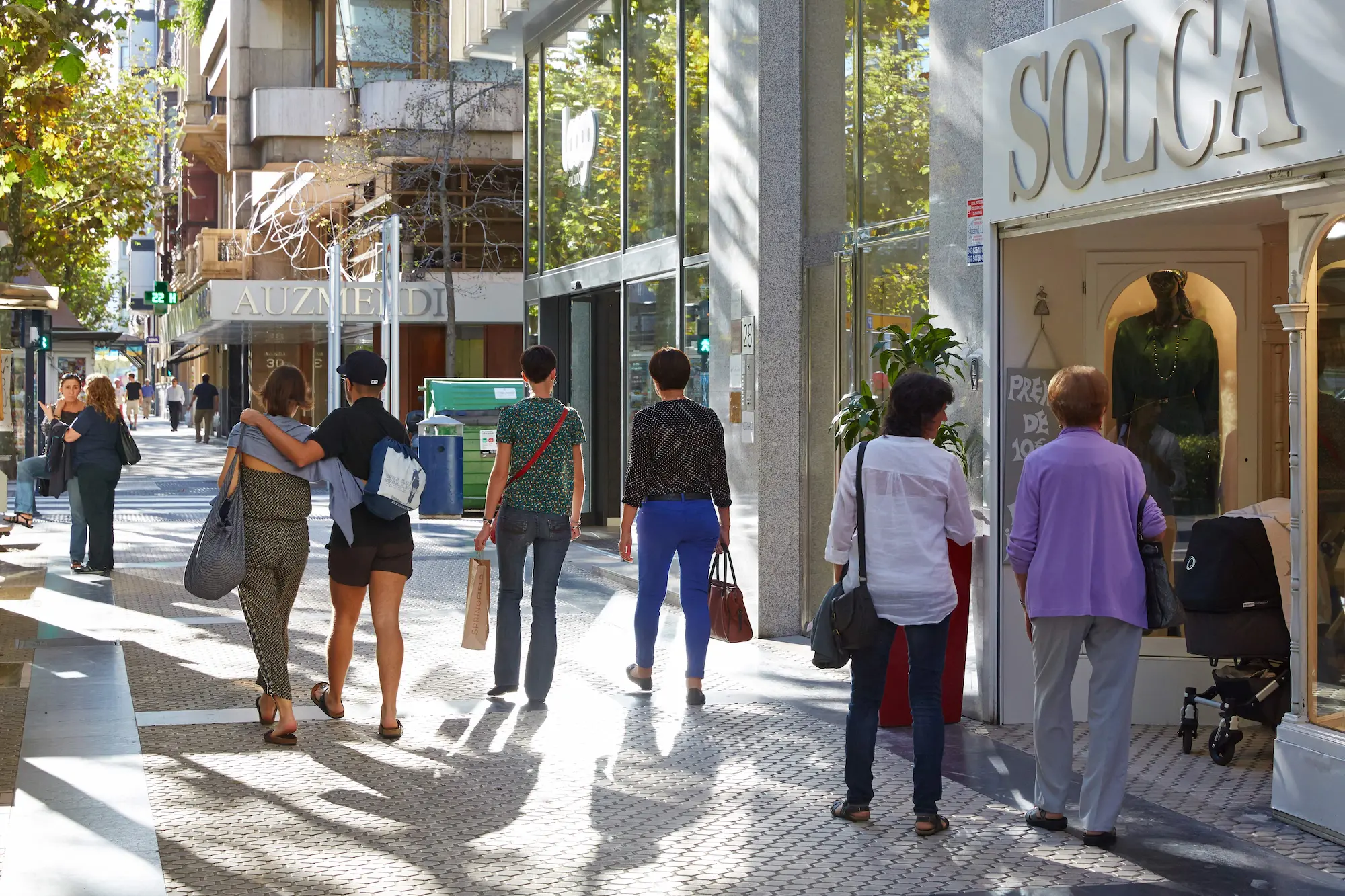 Personas caminando por la acera en la zona romántica de San Sebastián, disfrutando del ambiente urbano.