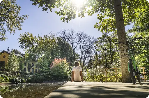 En el parque Cristina Enea, una persona observa el sol desde la acera, rodeada de la naturaleza del sitio.