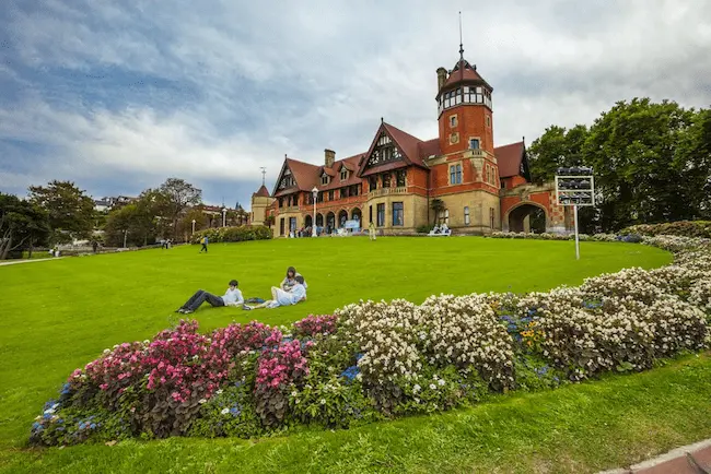 Vista del Palacio Miramar de San Sebastián, con personas acostadas en los jardines.