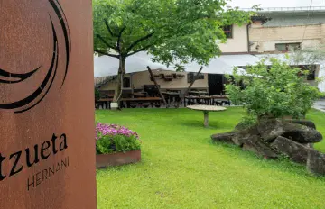 Jardín verde del albergue con mesas y bancos cubiertos al fondo