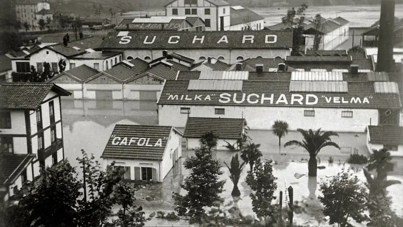 Foto antigua de la fábrica de chocolates Suchard, con un letrero visible, en medio de inundaciones en el Antiguo Bentaberri.