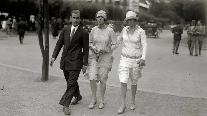 Hombre y dos mujeres caminando por la calle, luciendo moda de la época en la Diputación Foral de Gipuzkoa.