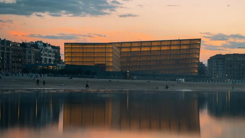 Vista del Kursaal en la playa durante el atardecer, con el cielo iluminado en tonos naranjas y rosas.