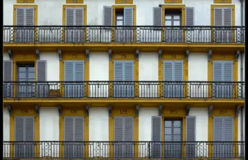 Fachada blanca y mostaza de pensión con balcones y contraventanas abiertas y cerradas