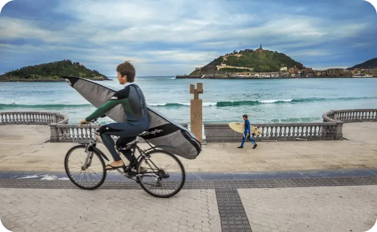 Child on a bike in a wetsuit with a surfboard along the promenade