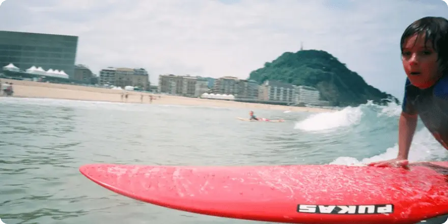 Niño surfeando una ola con tabla roja