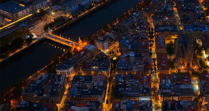 Vista panorámica nocturna de la Plaza Bilbao en San Sebastián, destacando su conexión mediante el Puente de María Cristina