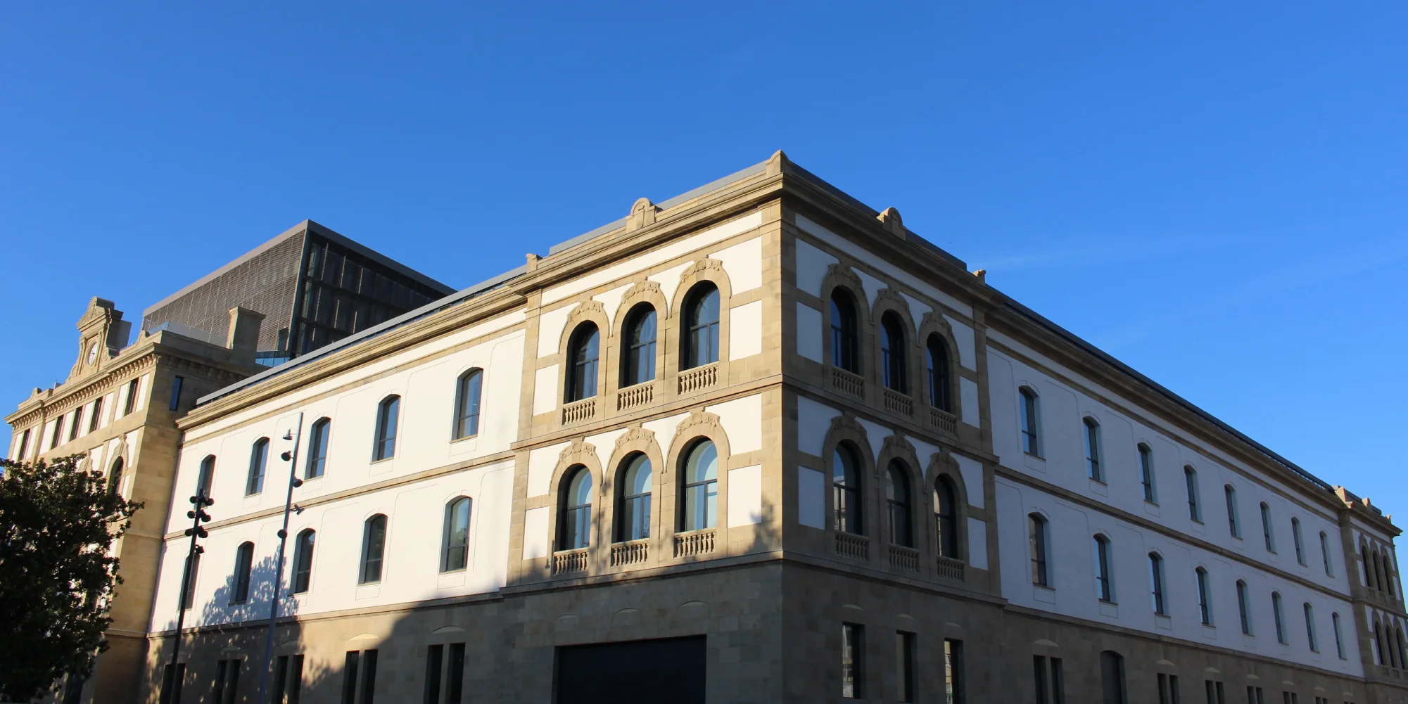 Un edificio de estilo clásico con paredes claras, una base de piedra y múltiples ventanas con arcos en la planta superior, bajo un cielo azul despejado.