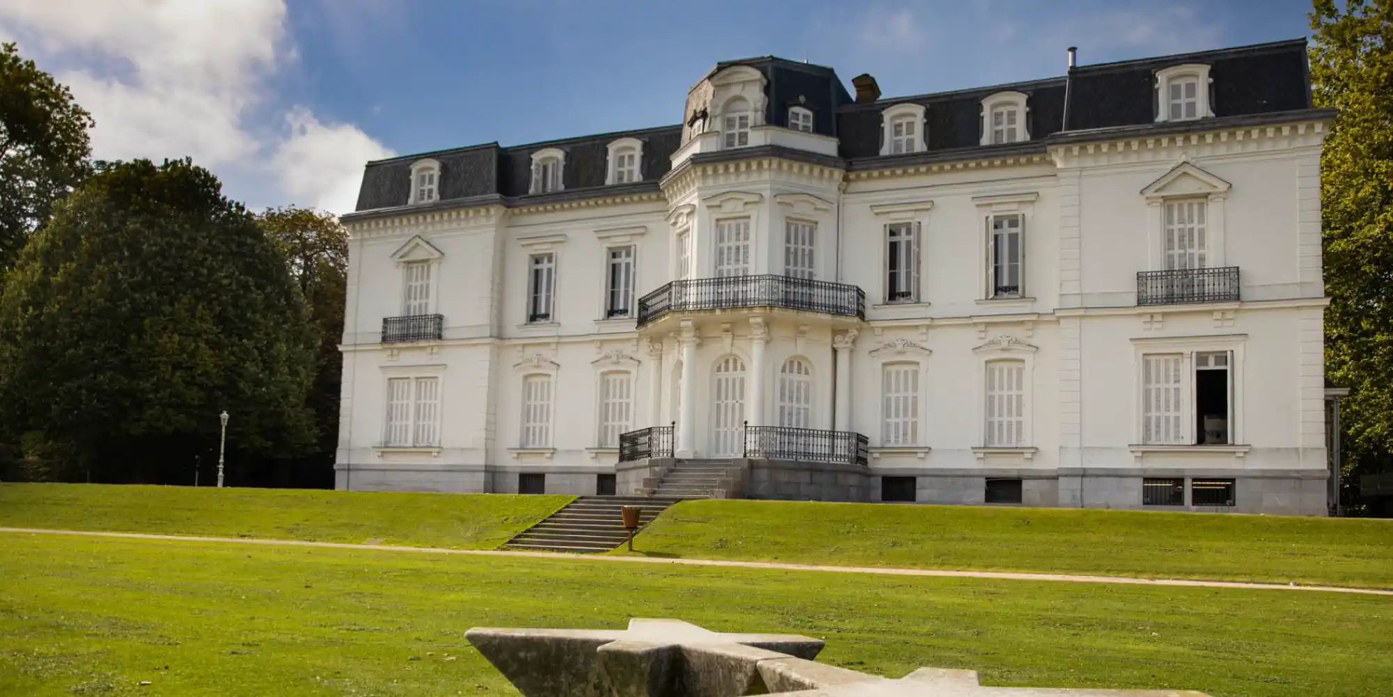 Una gran y elegante mansión blanca de estilo clásico con tejado oscuro, rodeada de césped verde y árboles en Aiete, San Sebastián.