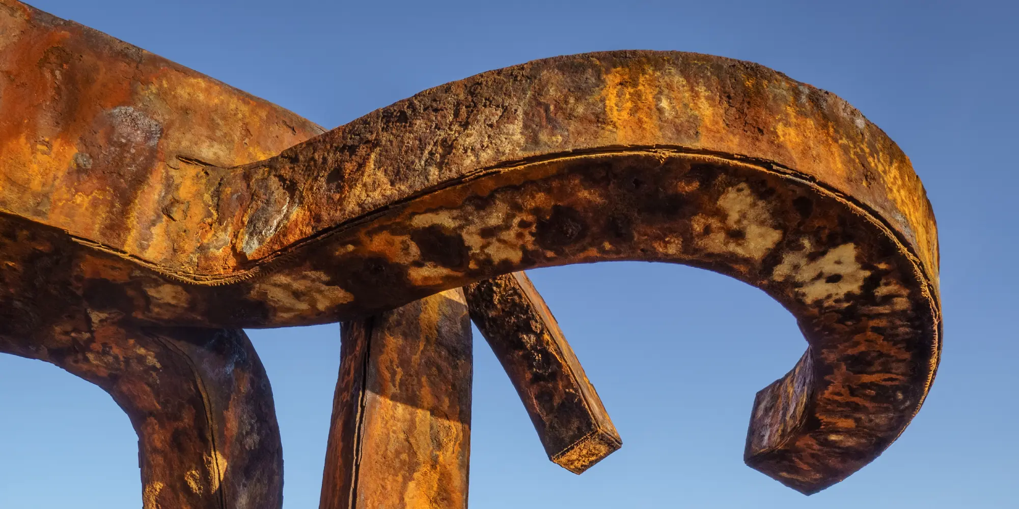Primer plano de la textura oxidada y las formas curvas de una de las esculturas de acero del "Peine del Viento" de Eduardo Chillida, contra un cielo azul claro, mostrando el arte y la intemperie del entorno marino de Donostia-San Sebastián.