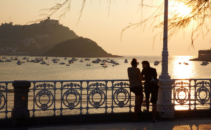 Pareja disfrutando del atardecer apollados en la barandilla de La Concha de Donostia / San Sebastián